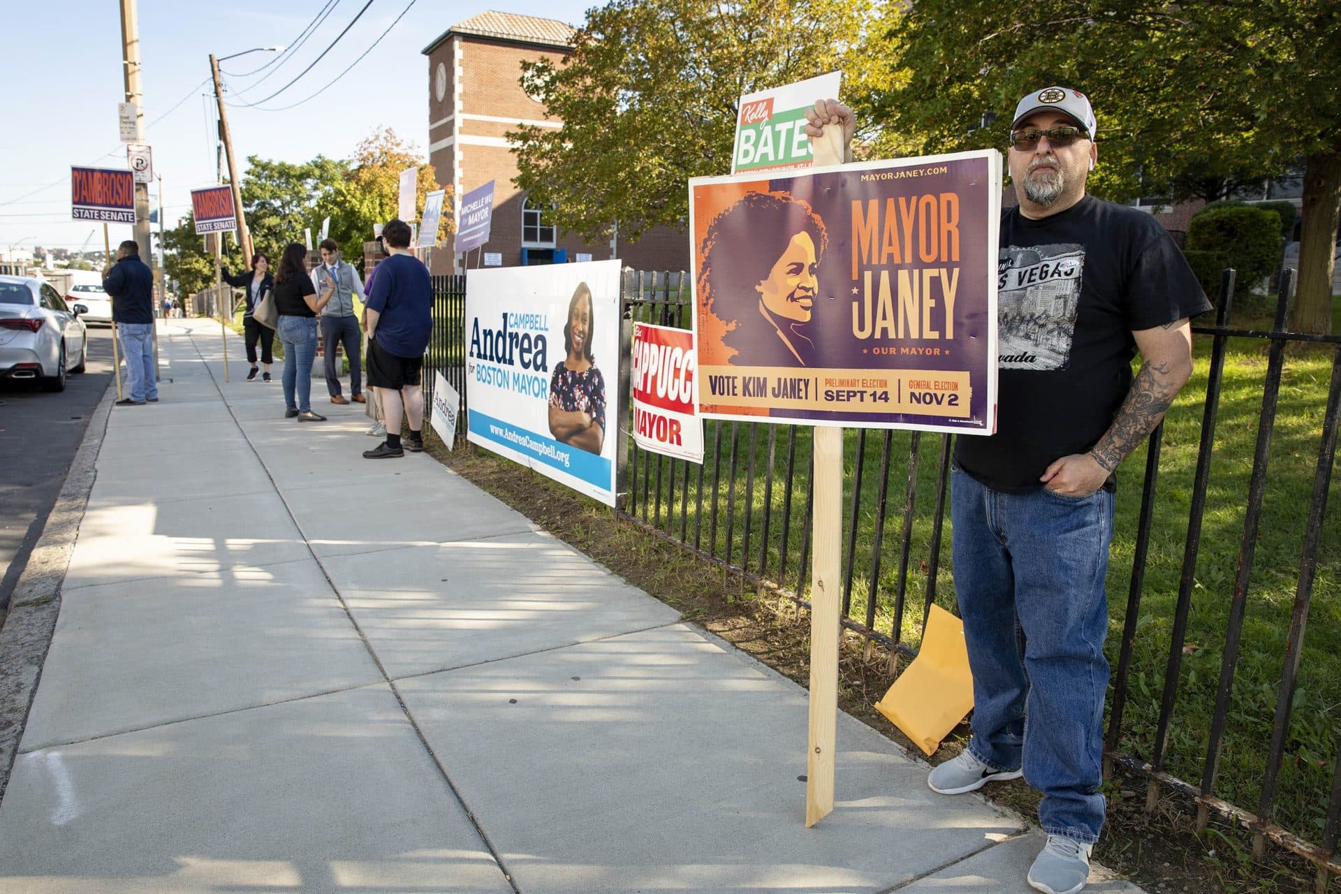 Larry Tinnirello holds up a "Vote Kim Janey" sign outside the East Boston High School polling location. (Robin Lubbock/WBUR)