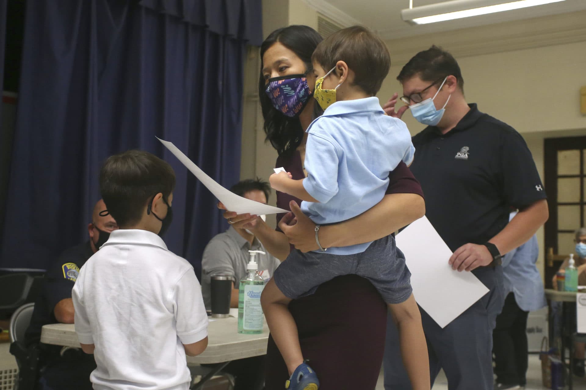 Michelle Wu, holding her 4-year-old son Cass, casts her ballot in the preliminary mayoral race on Tuesday, along with her husband, Conor Pewarski, and their other son, 6-year-old Blaise, at the Phineas Bates Elementary School in Boston. (Stew Milne/AP)