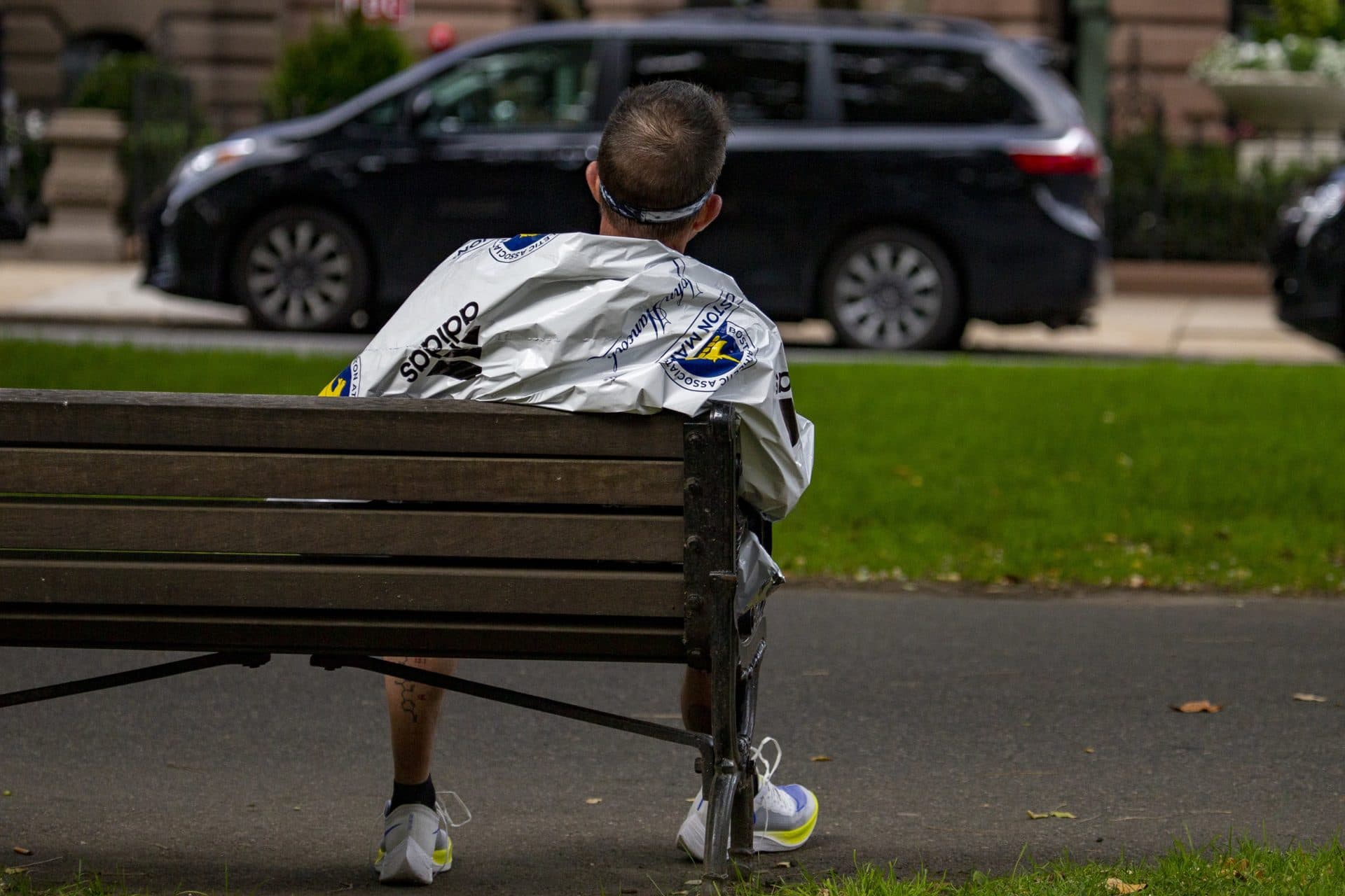 A marathon participant wrapped in a heatsheet blanket stits exhausted on a bench on the Commonwealth Mall after finishing the Boston Marathon. (Jesse Costa/WBUR)