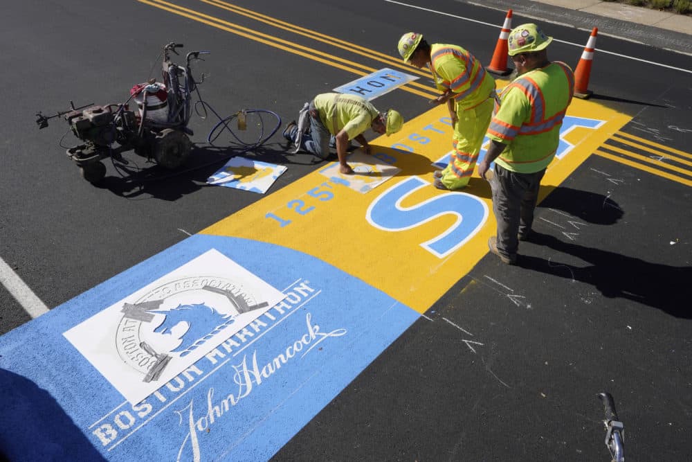 Painter Will Belezos, from Holbrook, left, uses a stencil on Wednesday, Oct.6, 2021, while working to complete the start line for the 125th annual Boston Marathon, at Hopkinton.  (Steven Senne / AP)