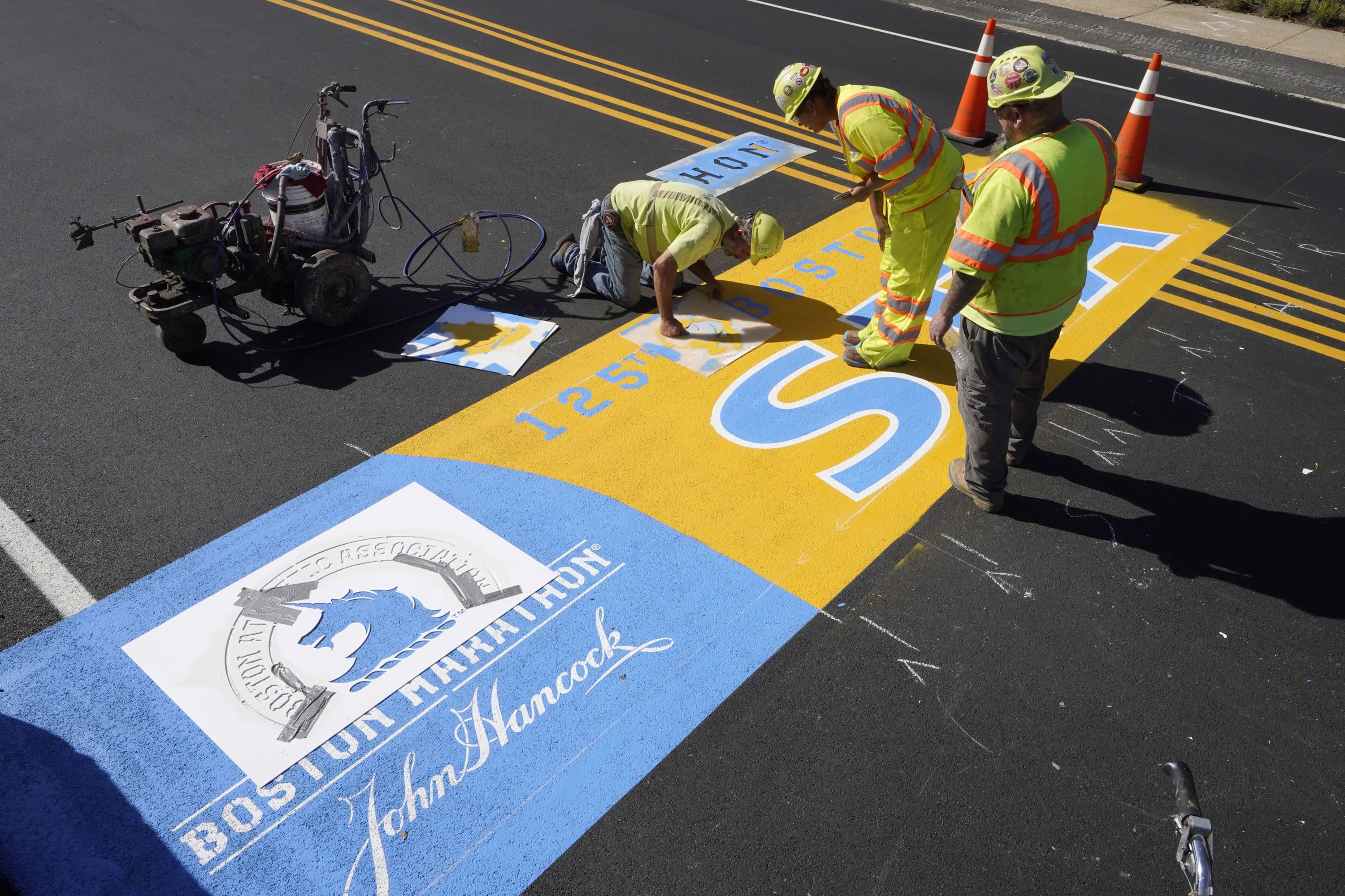 Painter Will Belezos, of Holbrook, left, uses a stencil, Wednesday, Oct 6, 2021, while working to complete the start line for the 125th edition of the Boston Marathon, in Hopkinton. (Steven Senne/AP)