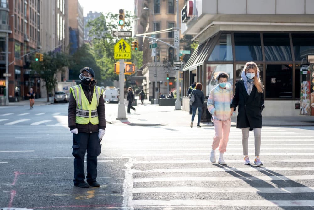 A school crossing guard stands in the street while a mother and child walk in the crosswalk on September 22, 2020 in New York City. (Alexi Rosenfeld/Getty Images)