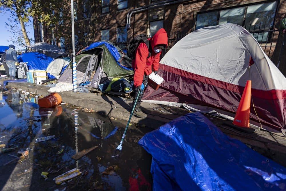 A Boston Public Health Commission worker collects a syringe from a puddle on Southampton Street during the clearing out of people living in tents in the "Masss and Cass" area. (Jesse Costa/WBUR)
