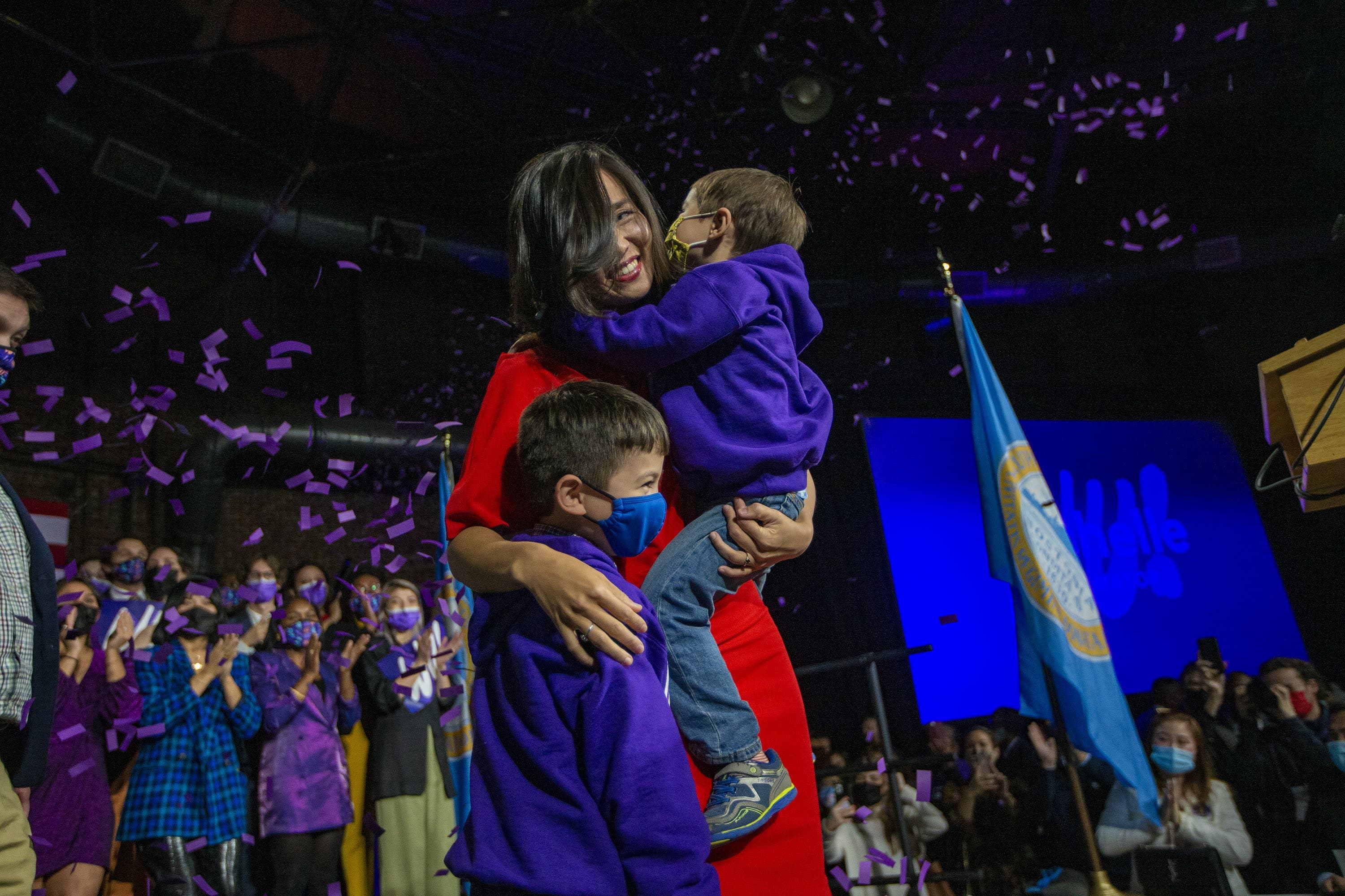 La recién elegida alcaldesa de Boston, Michelle Wu, abraza a sus hijos Cass y Blaise en el escenario del Cyclorama. (Jesse Costa / WBUR)