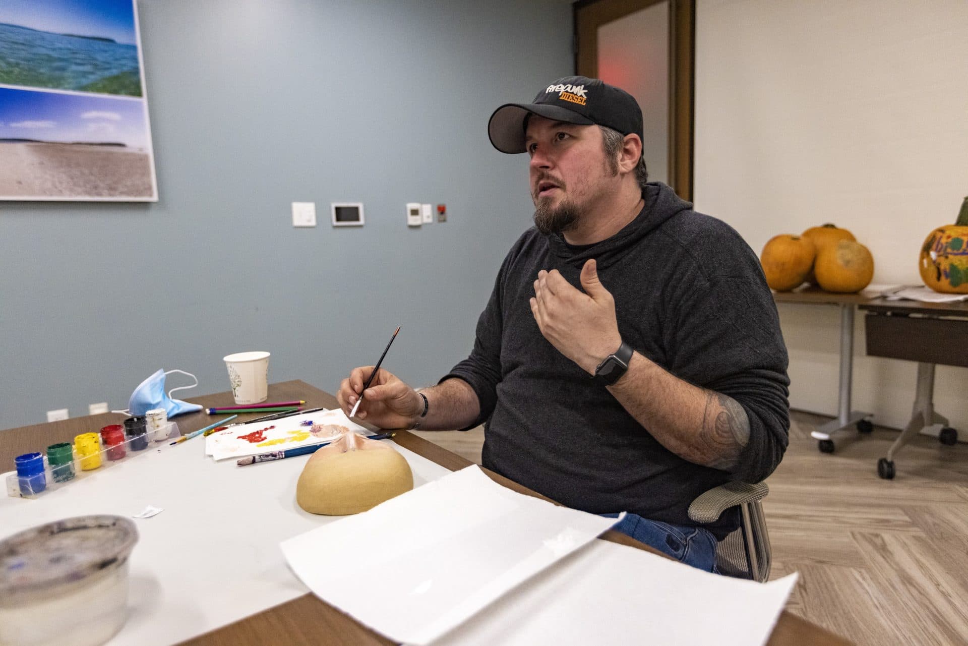 Air Force veteran John Hicks talks with Jennifer Kneeland, expressive art therapist and licensed mental health counselor, as he paints a mask. (Jesse Costa/WBUR)