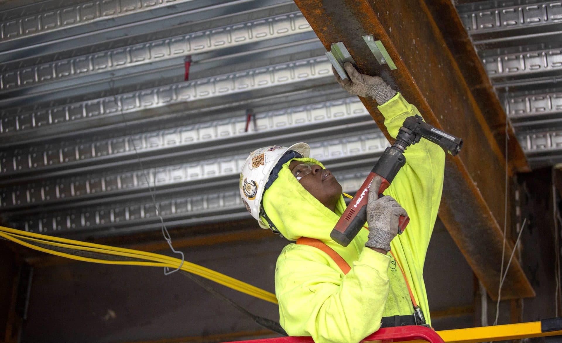 Angela Lormeus attaches metal brackets to a beam. (Robin Lubbock/WBUR)