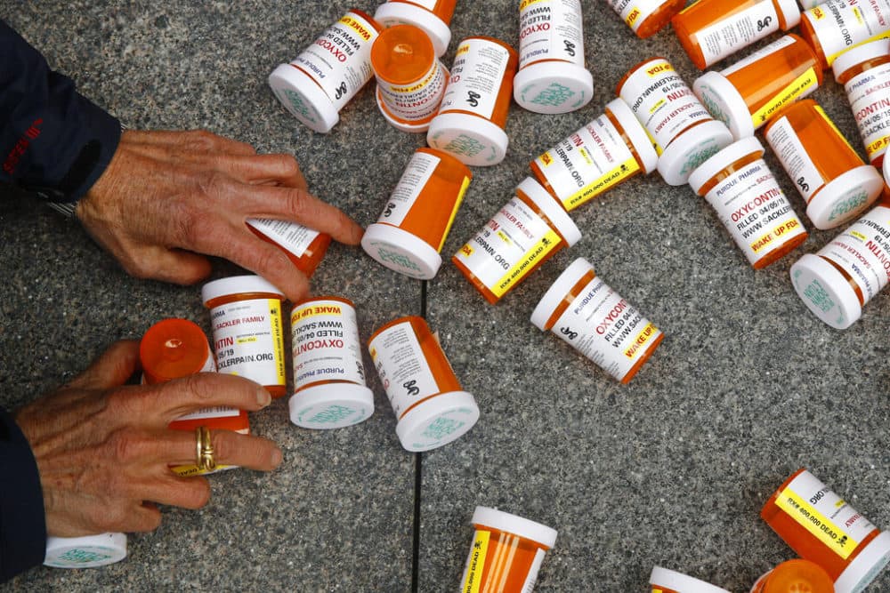 A protester gathers containers that look like OxyContin bottles at an anti-opioid demonstration in front of the U.S. Department of Health and Human Services headquarters in Washington on April 5, 2019. (AP Photo/Patrick Semansky, File)