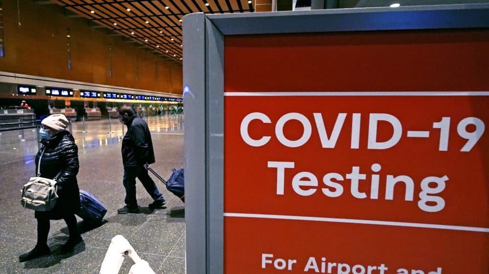 Travelers pass a sign near a COVID-19 testing site in Terminal E at Logan Airport, Dec. 21, 2021, in Boston. (Charles Krupa/AP)