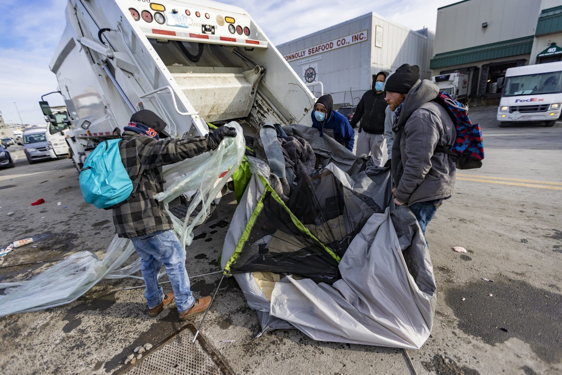 Workers throw part of a tent and debris into a garbage truck. (Jesse Costa/WBUR)