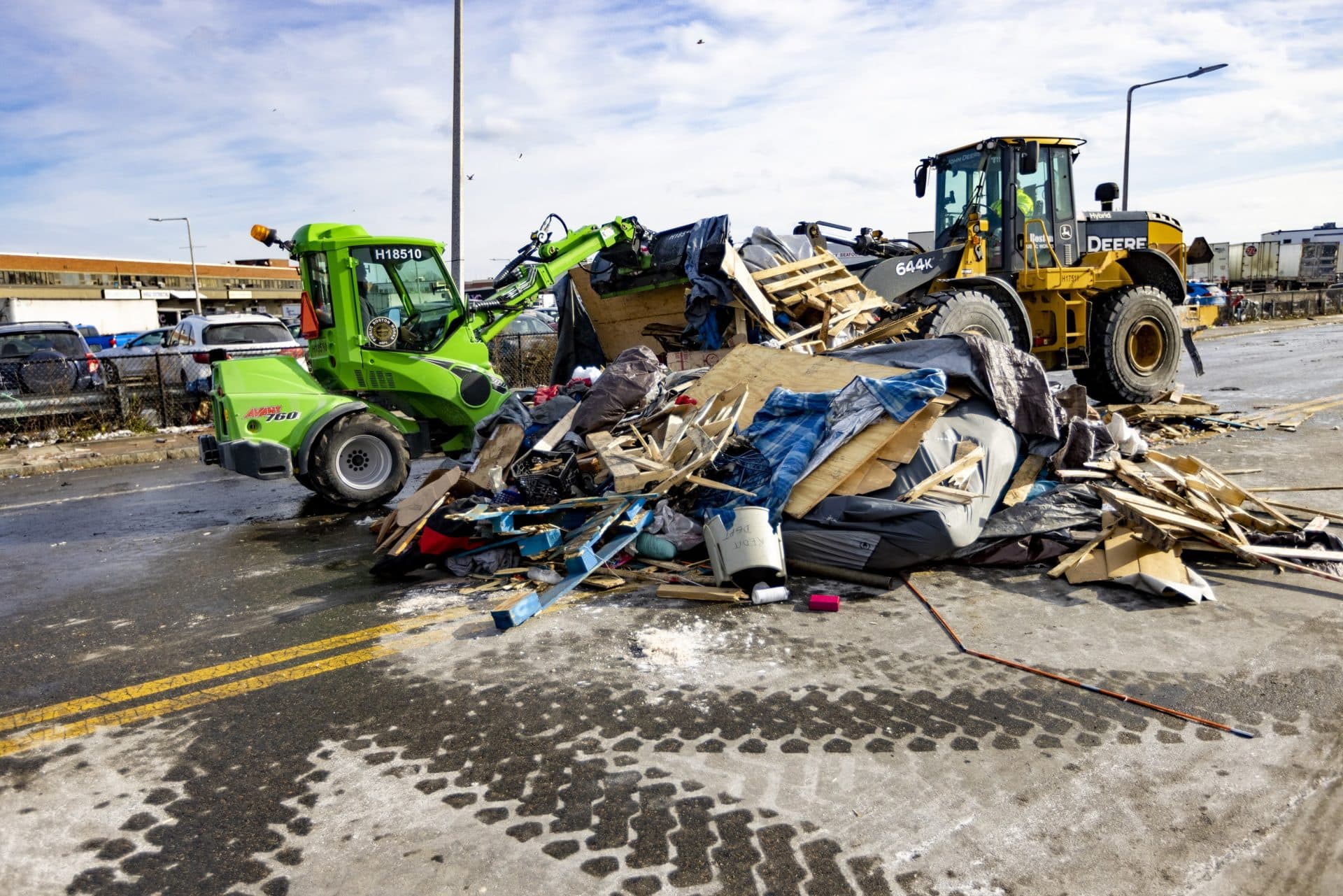 Two land mover trucks remove a pile of debris from the homeless encampment. (Jesse Costa/WBUR)
