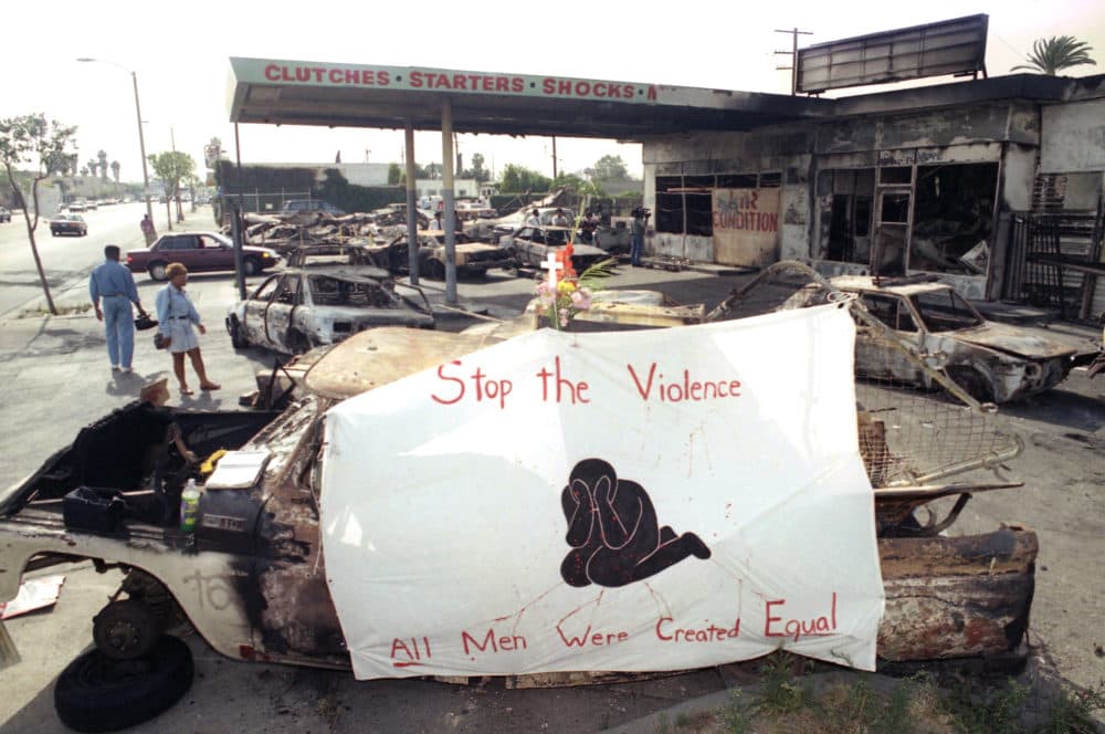 A cross, flowers and a banner urging an end to violence adorn the ruins of a service station at Florence and Normandie Avenues in South-Central Los Angeles, May 3, 1992. The intersection was the site of the first reported violence on Wednesday that led to days of rioting, looting and burning as people angrily reacted to the acquittal of four Los Angeles police officers in the Rodney King assault. (Reed Saxon/AP)