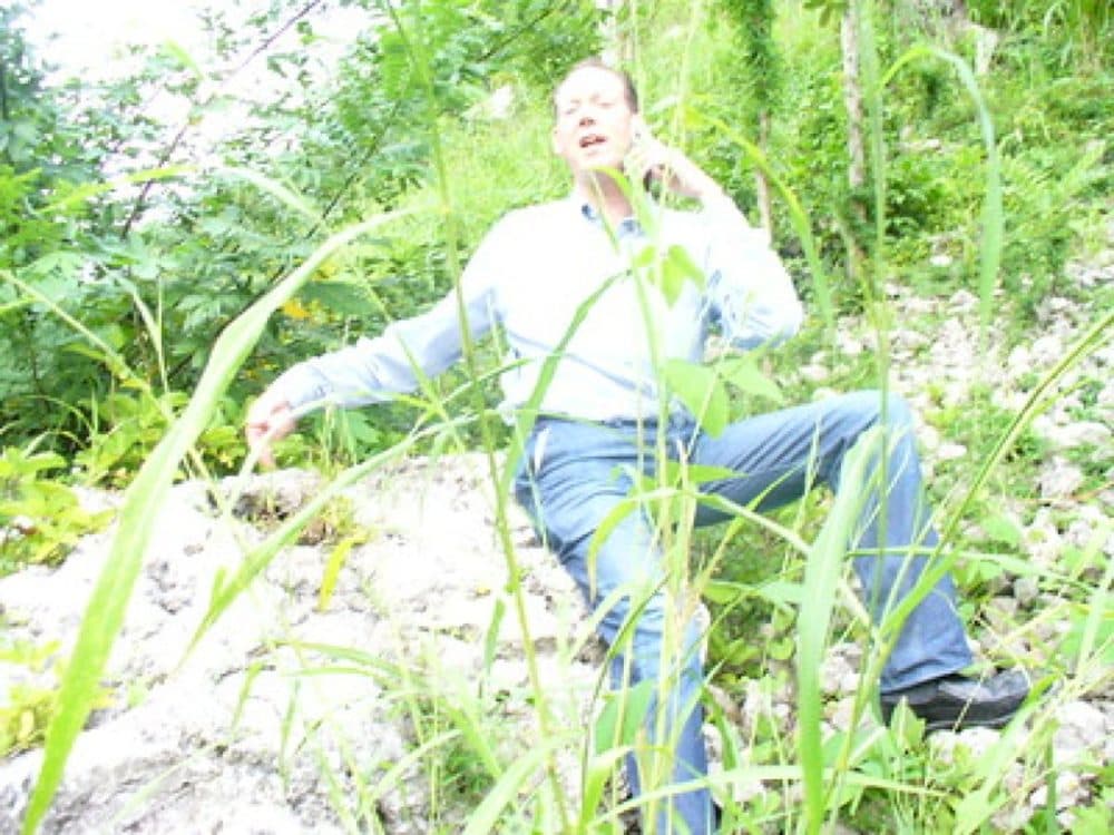 Dr. Paul Farmer on the phone, while seated on 'the rock' on the side of the road, that would become a centerpiece of a hospital garden. (Courtesy Monika Kalra Varma)