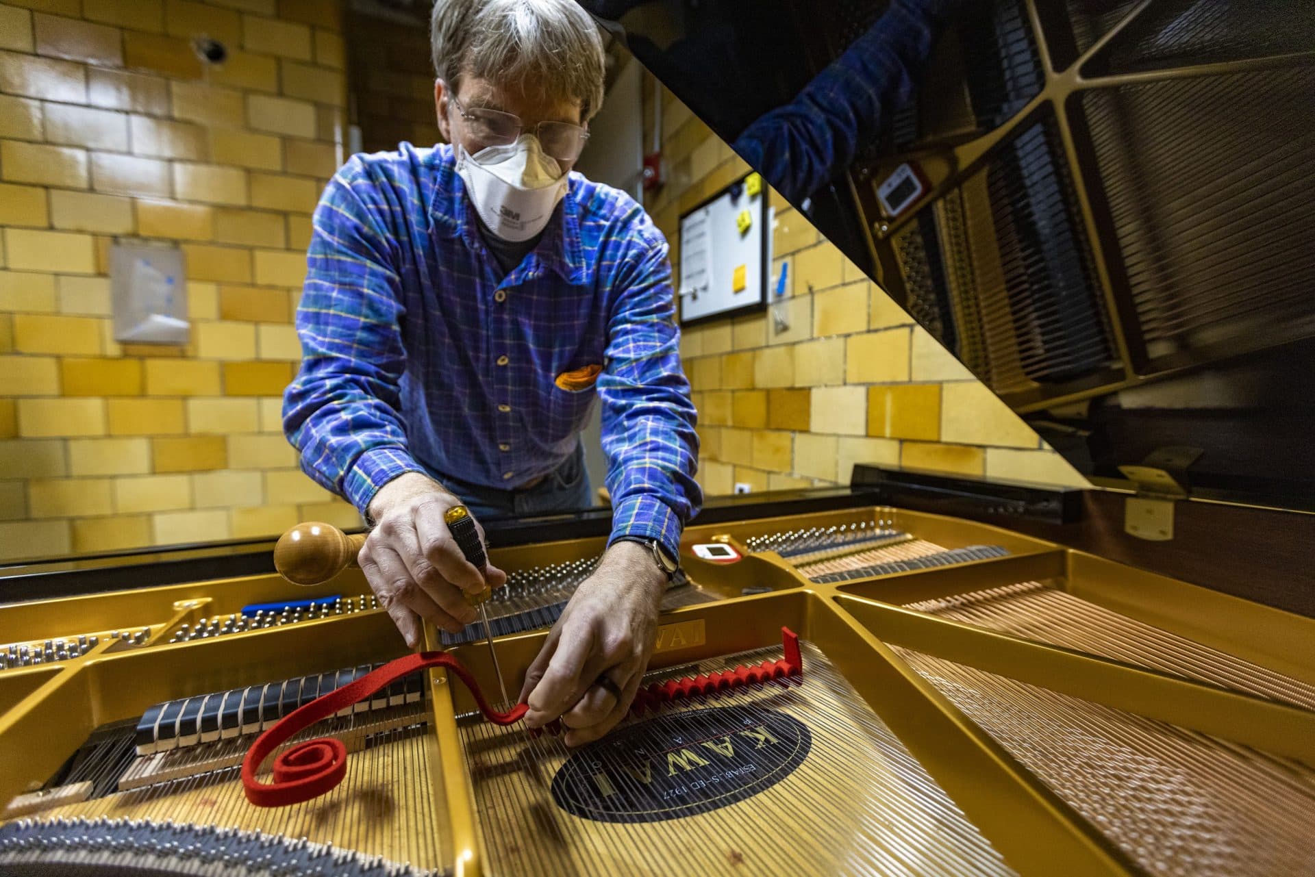 Michael Carlin places piano tuning felt between the strings of an instrument used for training in the piano technology program at North Bennet Street School. Carlin wants to become a piano tuner after a long career as an immigration attorney. (Jesse Costa/WBUR)
