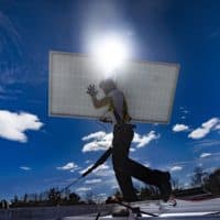 A technician walks with a solar panel across the rooftop during a solar panel installation at Boston Building Resources in Jamaica Plain. (Jesse Costa/WBUR)