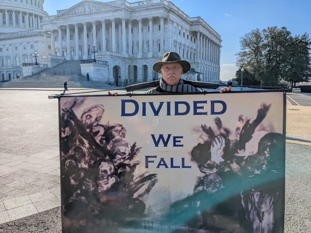 Stephen Parlato, an artist and activist, protests with signs outside of the Capitol building in Washington, D.C. (James Perkins Mastromarino/Here & Now)