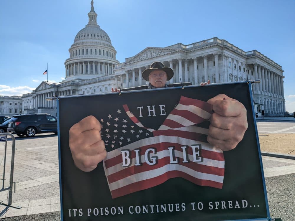 Stephen Parlato, an artist and activist, protests with signs outside of the Capitol building in Washington, D.C. (James Perkins Mastromarino/Here & Now)