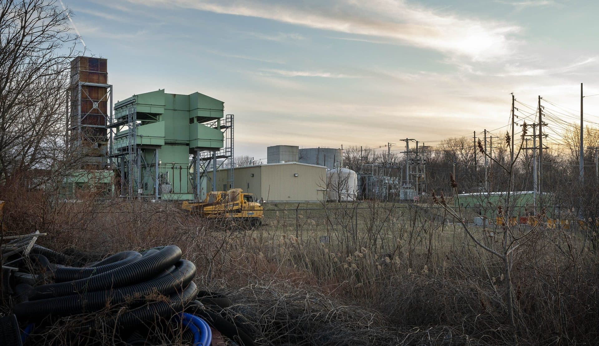 The plot on Pulaski Street currently has two gas peaker power plants. The proposed third plant would be built in the flat grassy area where the two yellow trucks are parked. (Robin Lubbock/WBUR)