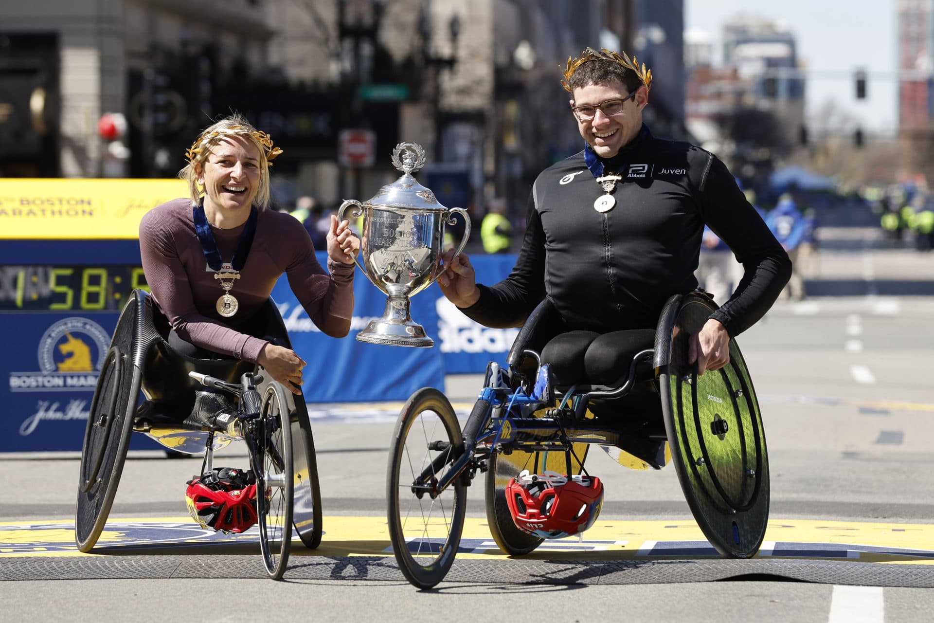 Manuela Schar of Switzerland (left) and Daniel Romanchuck of the United States hold the trophy after winning the men's and women's wheelchair divisions.  (Winslow Townson/AP)