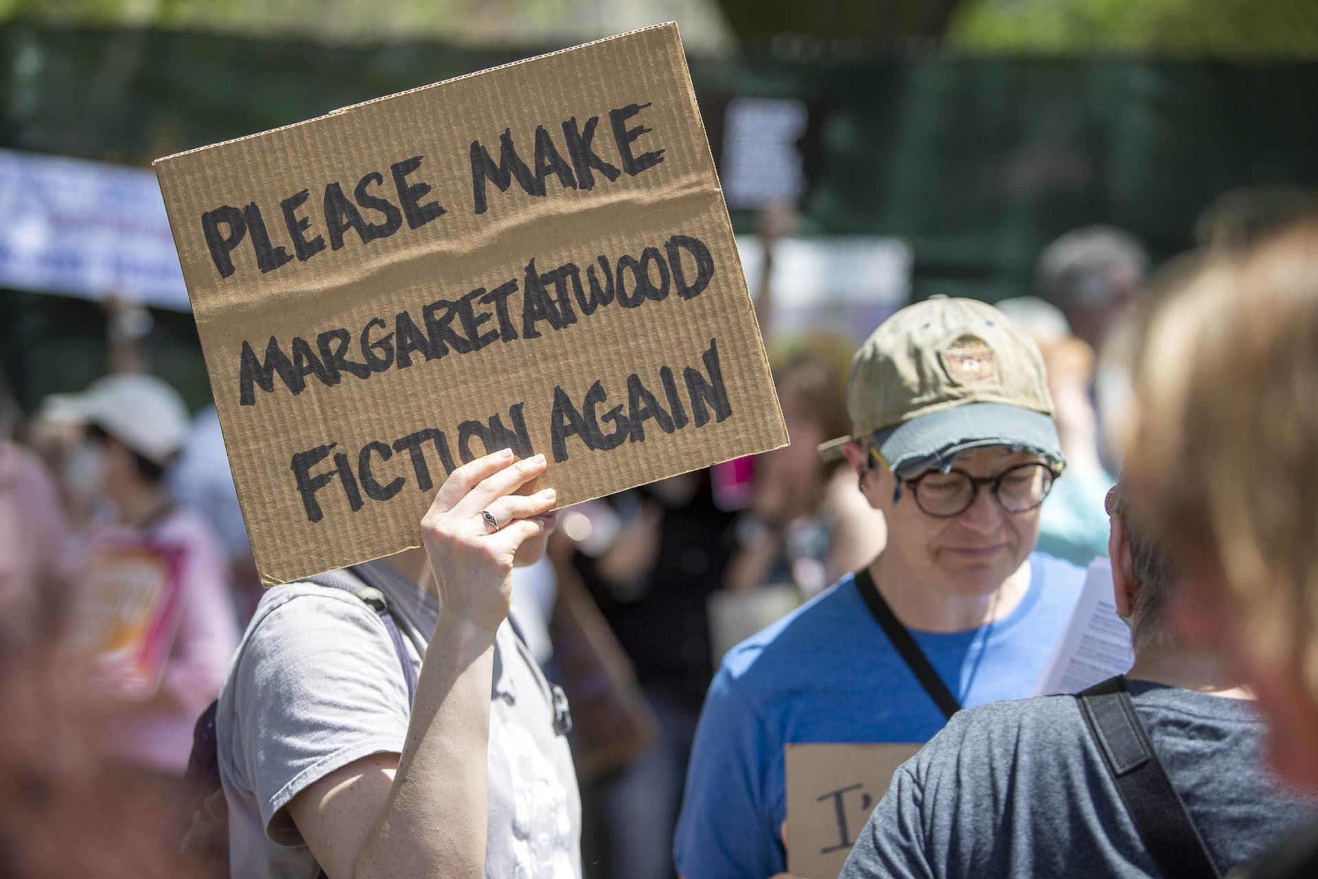 A protester holds up a sign saying "Please Make Margaret Atwood Fiction Again" at the Bans Off Our Bodies rally on Boston Common. (Robin Lubbock/WBUR)