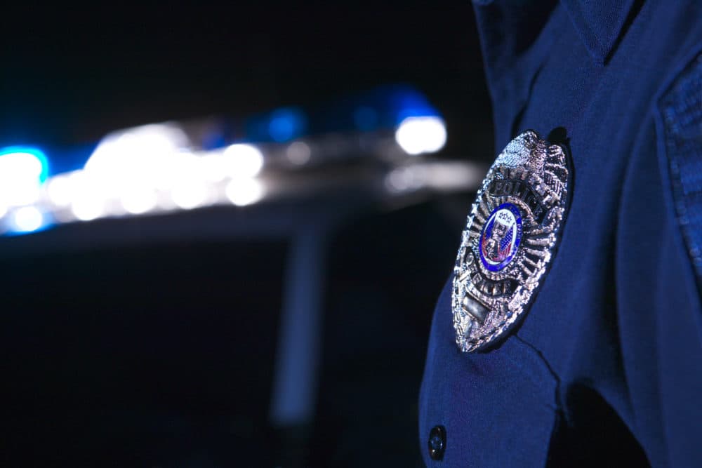 Close-up of an officer's badge with the police lights on the car flashing in the background. (Getty Images) 