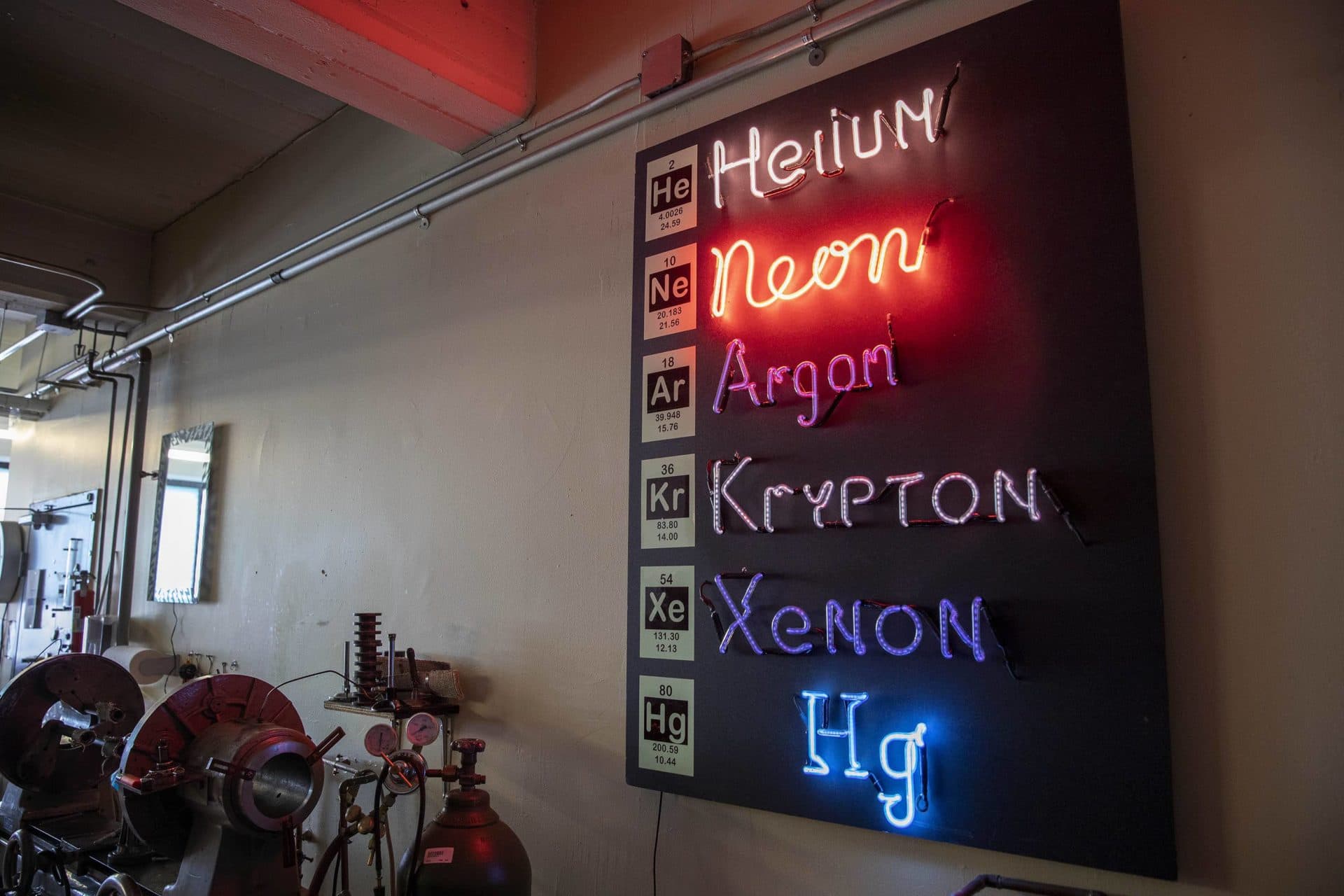 A sign on the wall of Wayne Strattman's studio shows the different colors of the plasma of different gases.  (Robin Lubbock / WBUR)