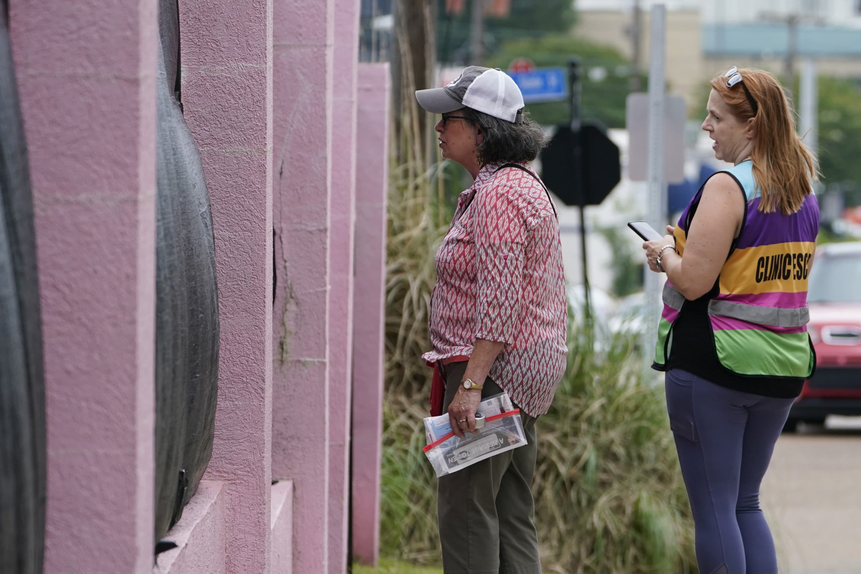 Pam Miller, an anti-abortion sidewalk counselor, left, speaks through the tarp draped fencing of the Jackson Womens Health Organization clinic, to an incoming patient at the front of the "Pink House," while clinic escort Kim Gibson counters her statements, Thursday, May 20, 2021, in Jackson, Miss. (Rogelio V. Solis/AP)